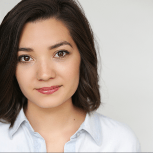 headshot of a woman with fair skin and dark brown, shoulder-length hair and brown eyes, wearing a collared light blue top, in front of a white background